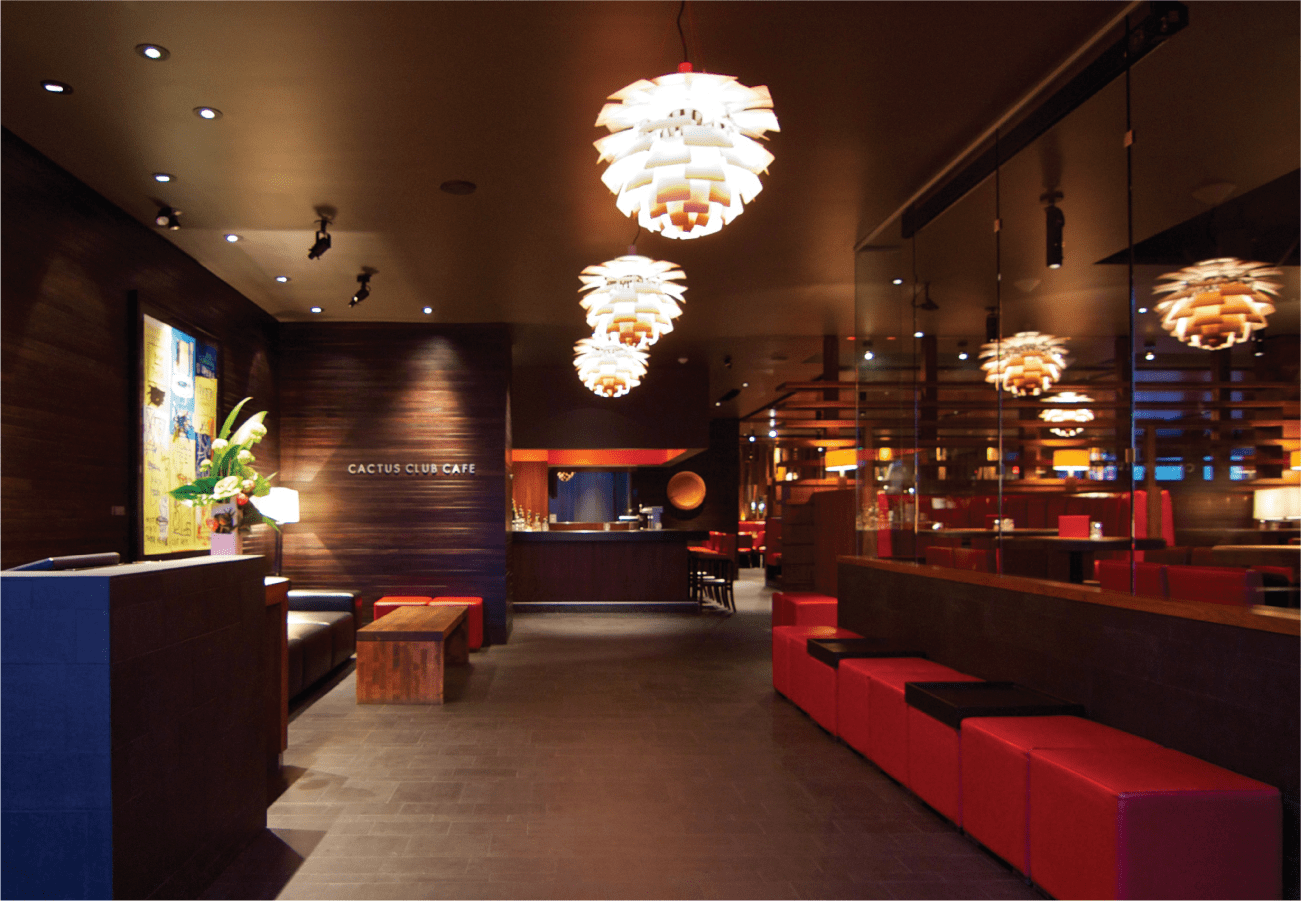Cactus Club Cafe interior in Burnaby featuring modern pendant lighting, red seating, dark wood accents, and an illuminated sign at the reception area