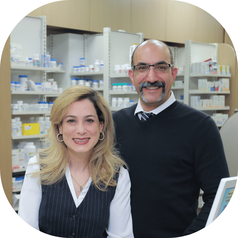 Two pharmacists smiling at the camera in a Burnaby pharmacy with medication shelves in the background