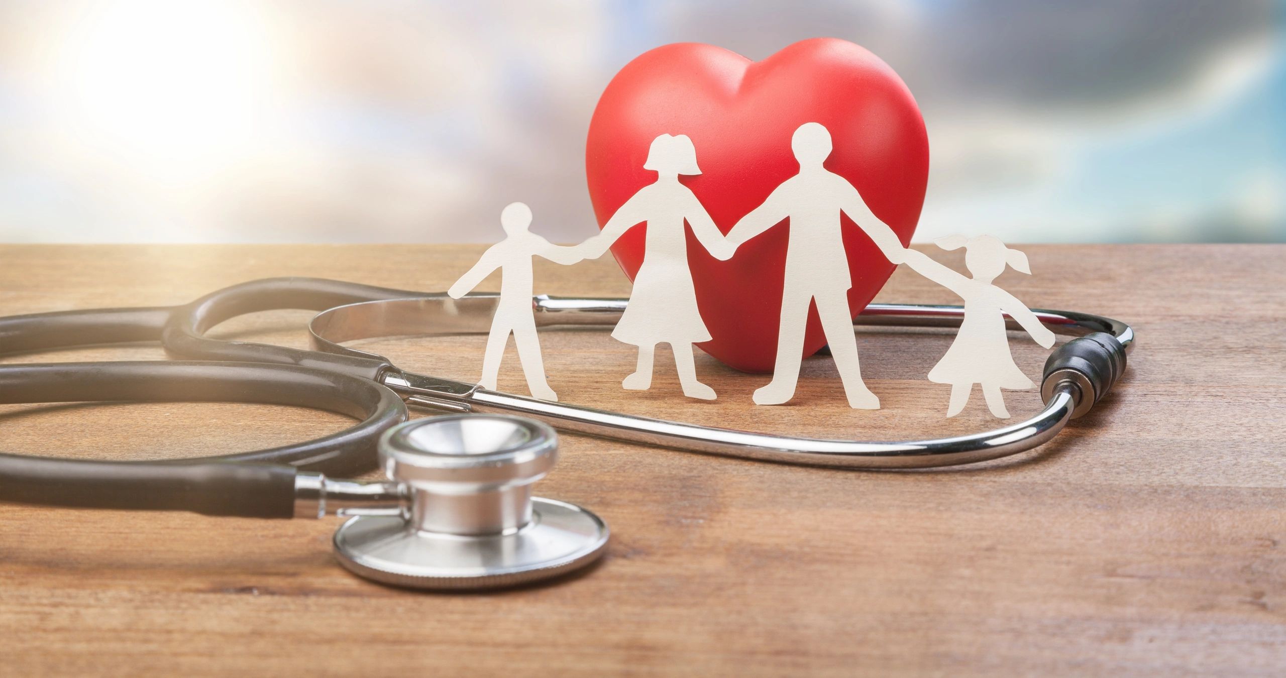 Paper cutout family figures holding hands behind a red heart with a stethoscope on a wooden surface, representing family health care at MedCare Plus Medical Clinic in Burnaby