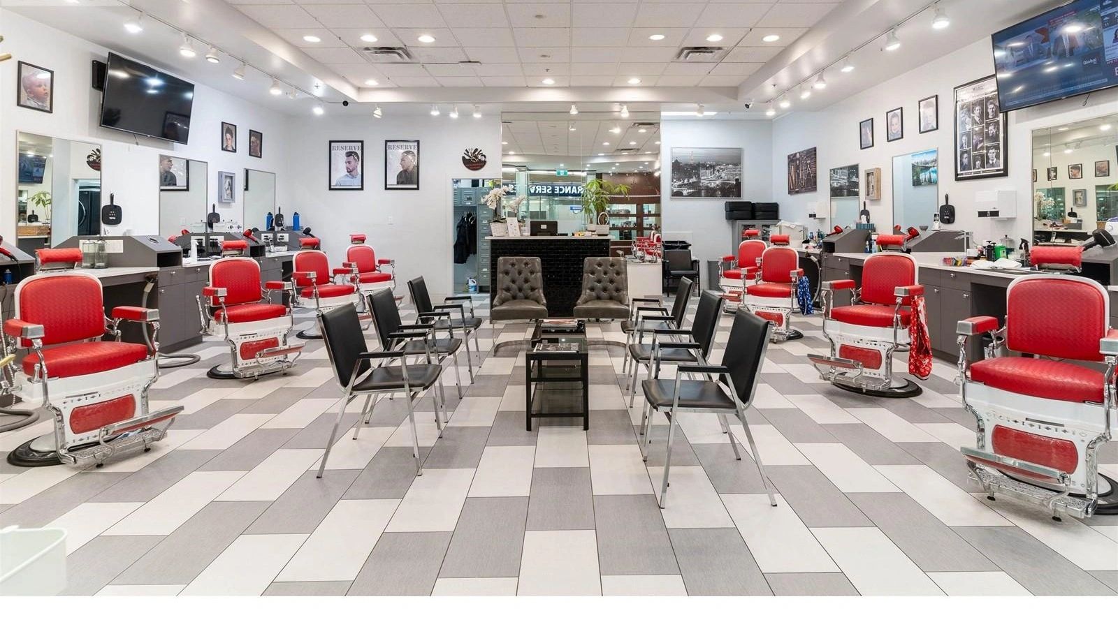 Modern barbershop interior in Burnaby with red barber chairs, black waiting chairs, and geometric flooring