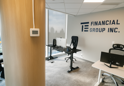 Modern office space at TE Financial Group Inc. in Burnaby featuring a wooden accent wall, black ergonomic office chairs, desks with computers, and the company logo on the wall