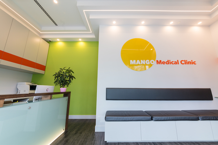 Mango Medical Clinic reception area in Burnaby featuring a bright lime green accent wall, modern white cabinetry, and the clinic's logo with a yellow mango icon and red text on a white wall