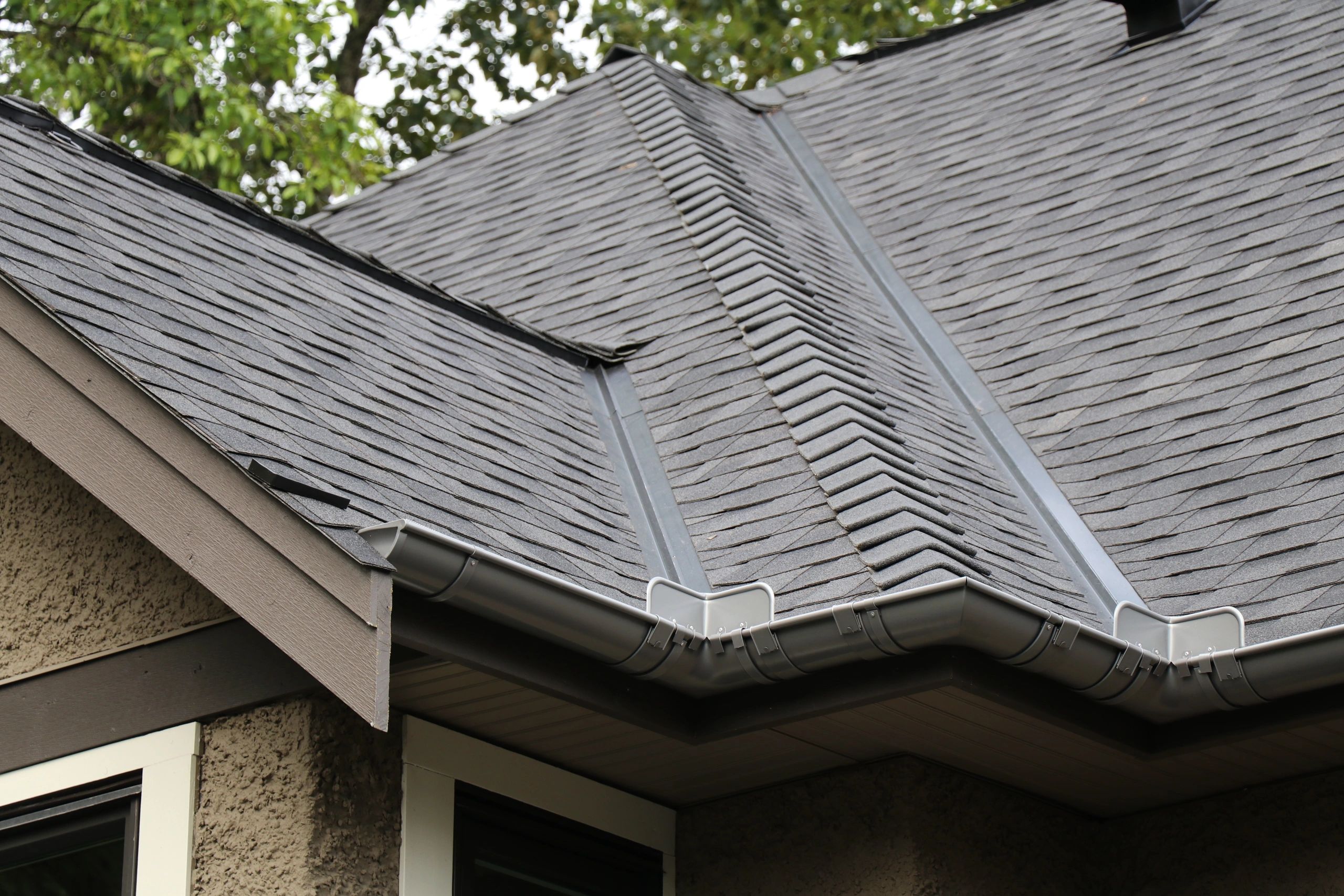 Close-up view of a residential roof in Burnaby featuring gray asphalt shingles with a clean gutter system and downspout