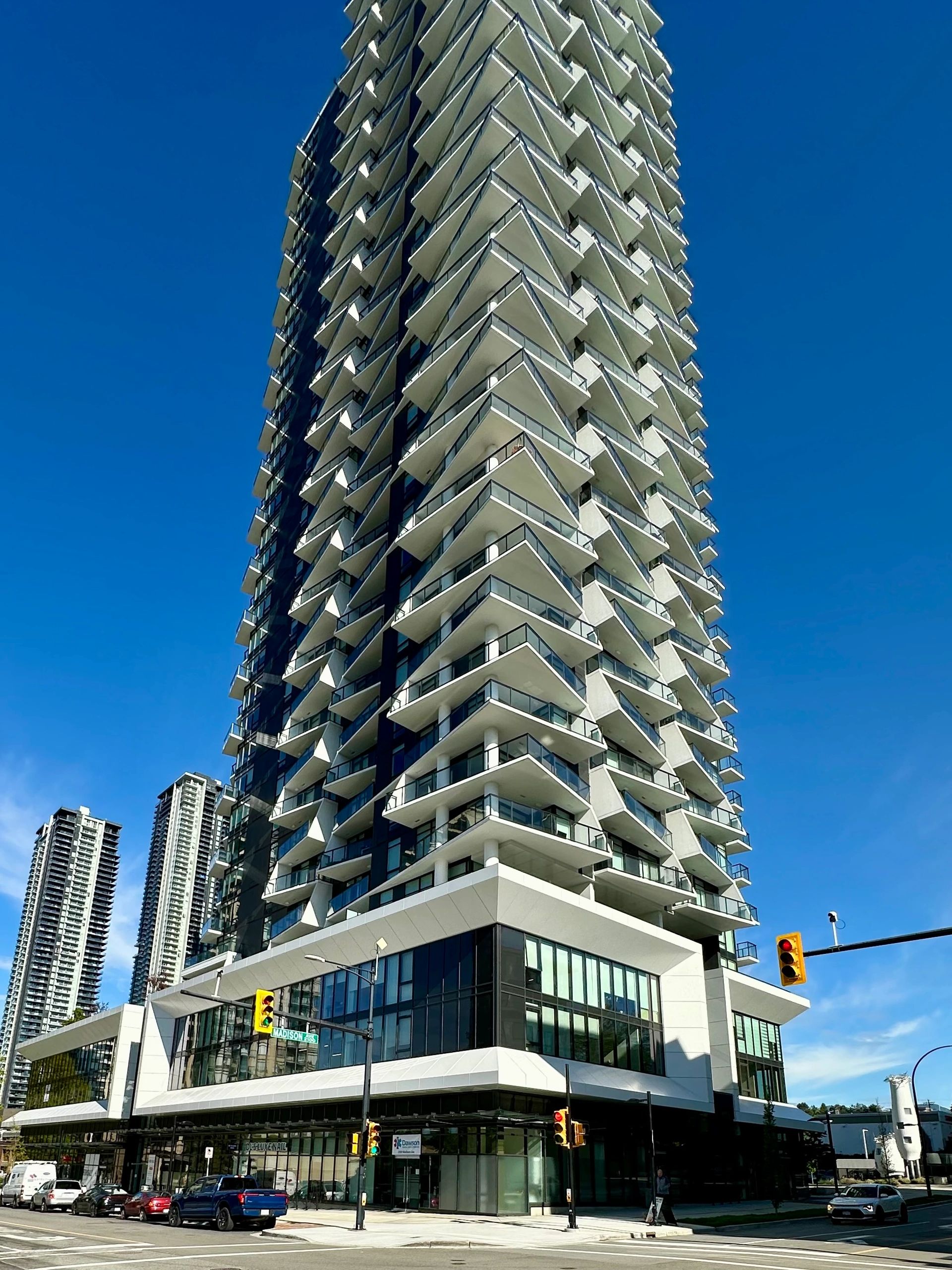 Tall modern residential high-rise building with white balconies and glass ground-floor commercial space in Burnaby, British Columbia