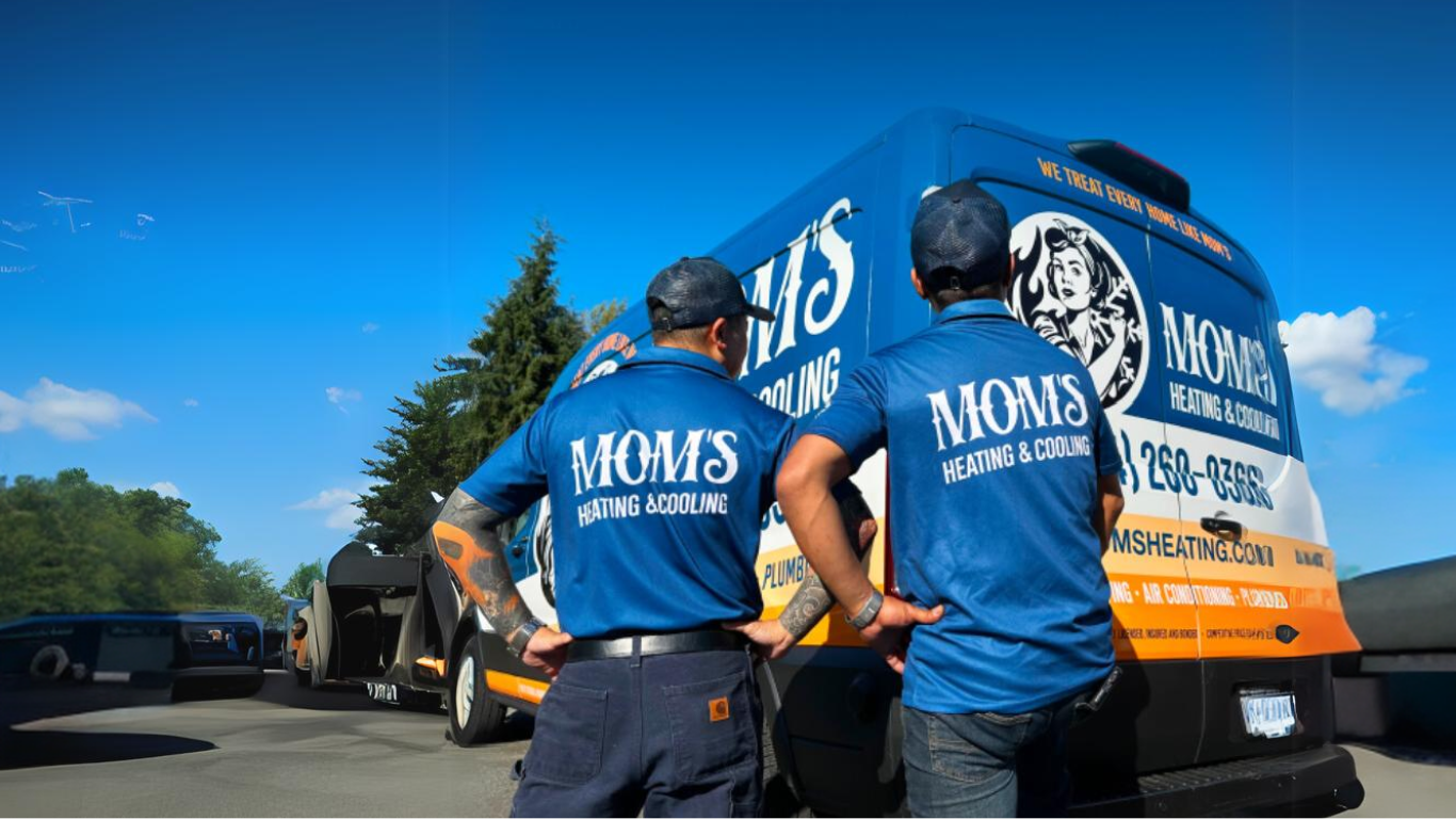 Three service technicians wearing blue Mom's Heating & Cooling uniforms standing in front of branded service vehicles in Burnaby