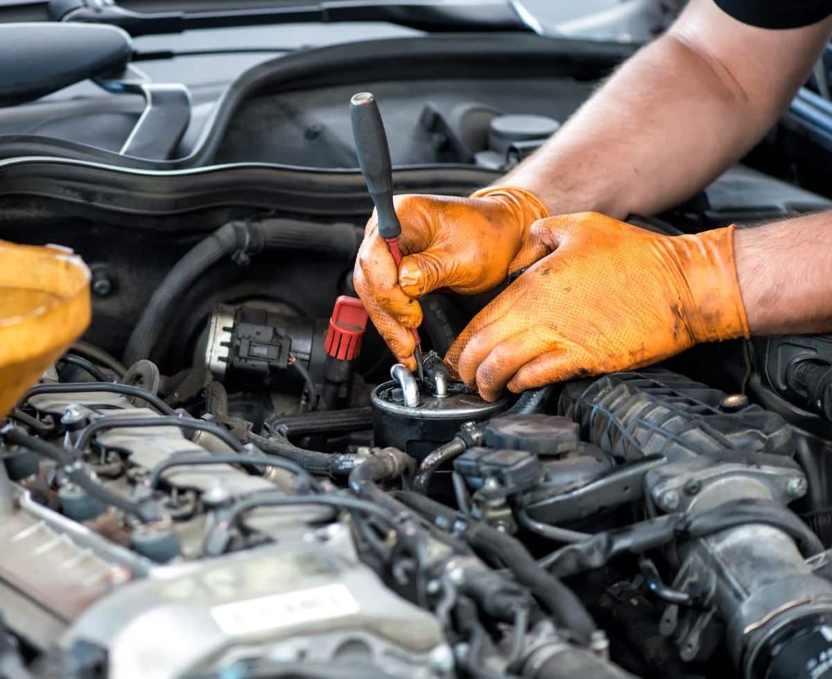 Mechanic in orange work gloves using a wrench to service an engine at Bill & Walter's Garage Ltd in Burnaby