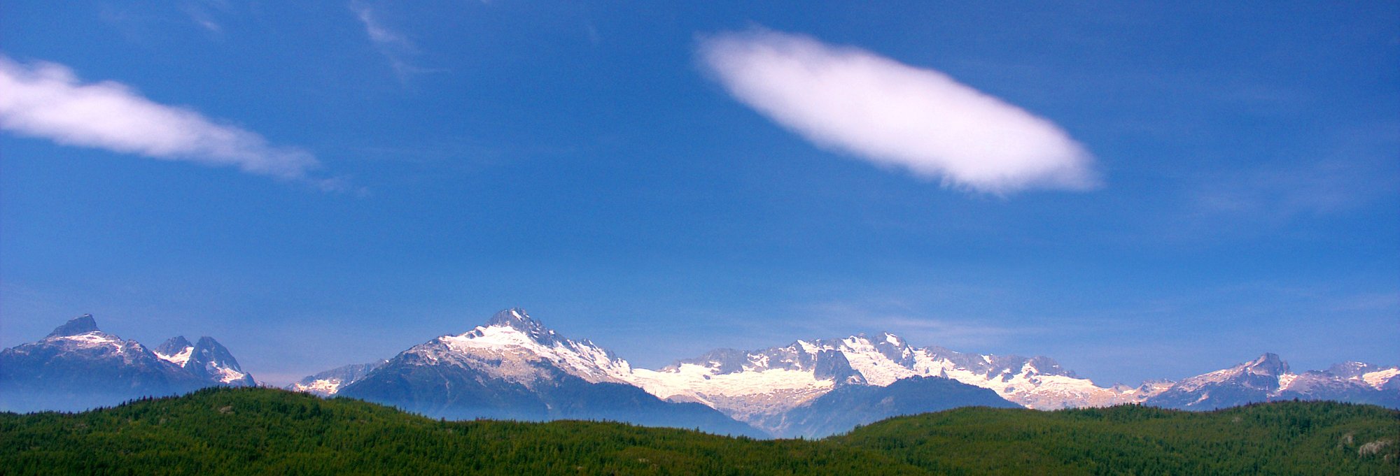 Snow-capped mountain range with forested foothills under blue sky, representing the natural beauty near Burnaby
