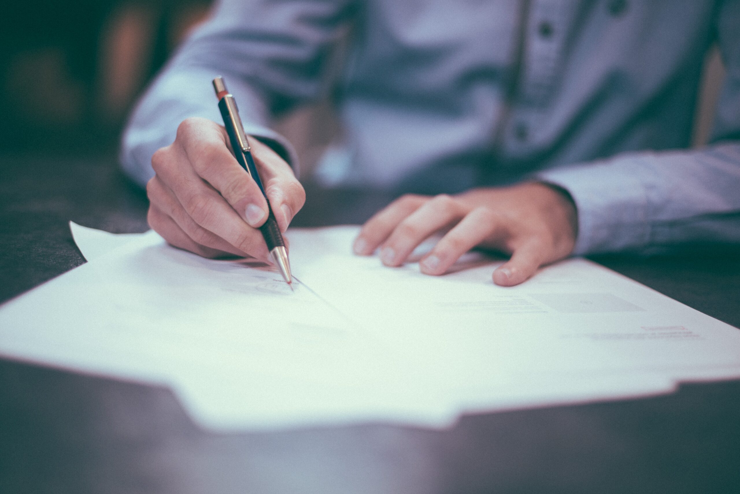 Person in business attire writing with a pen on a blank document at a table, representing professional accounting and financial services in Burnaby Heights