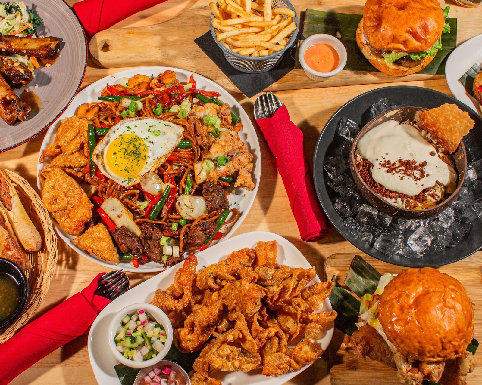 Overhead view of a table of Halina dishes, with Pancit Batil Patong under a fried egg, crispy chicken skin, wings and burgers